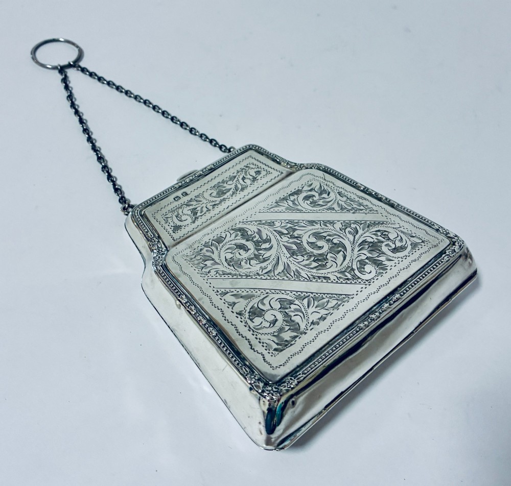 An antique sterling silver evening purse featuring engraved floral scrollwork, visible hallmarks along the upper frame, and a chain handle with a finger ring. View VI