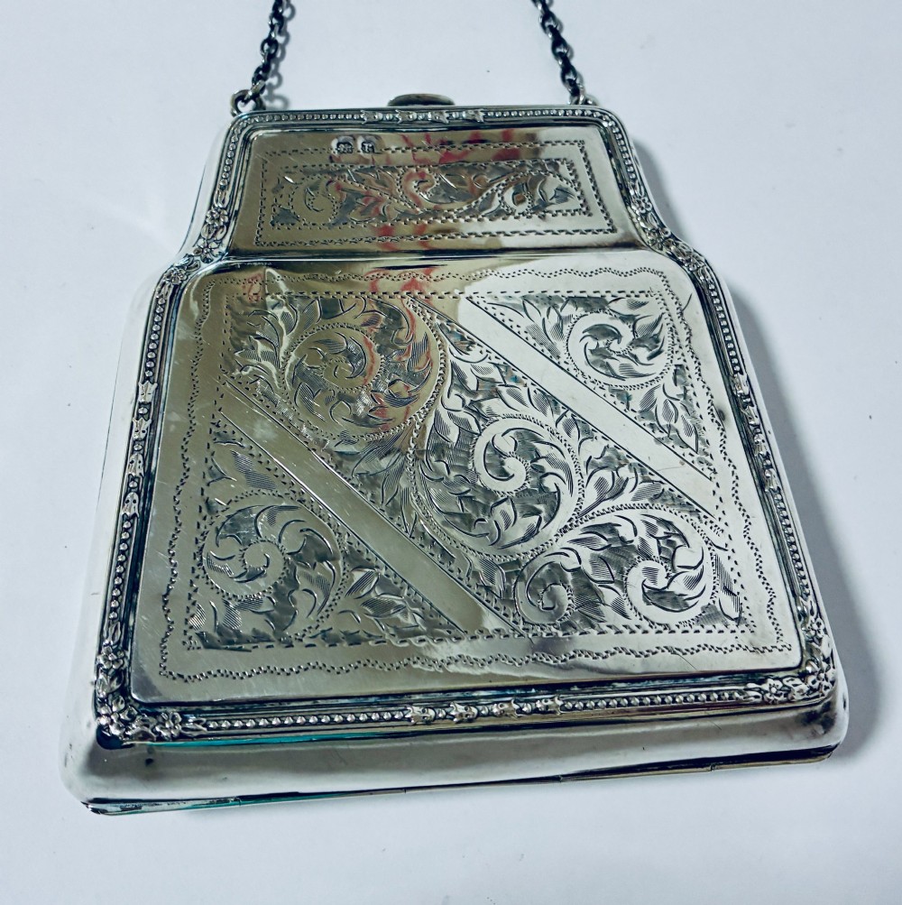 An antique sterling silver evening purse featuring engraved floral scrollwork, visible hallmarks along the upper frame, and a chain handle with a finger ring. View VII