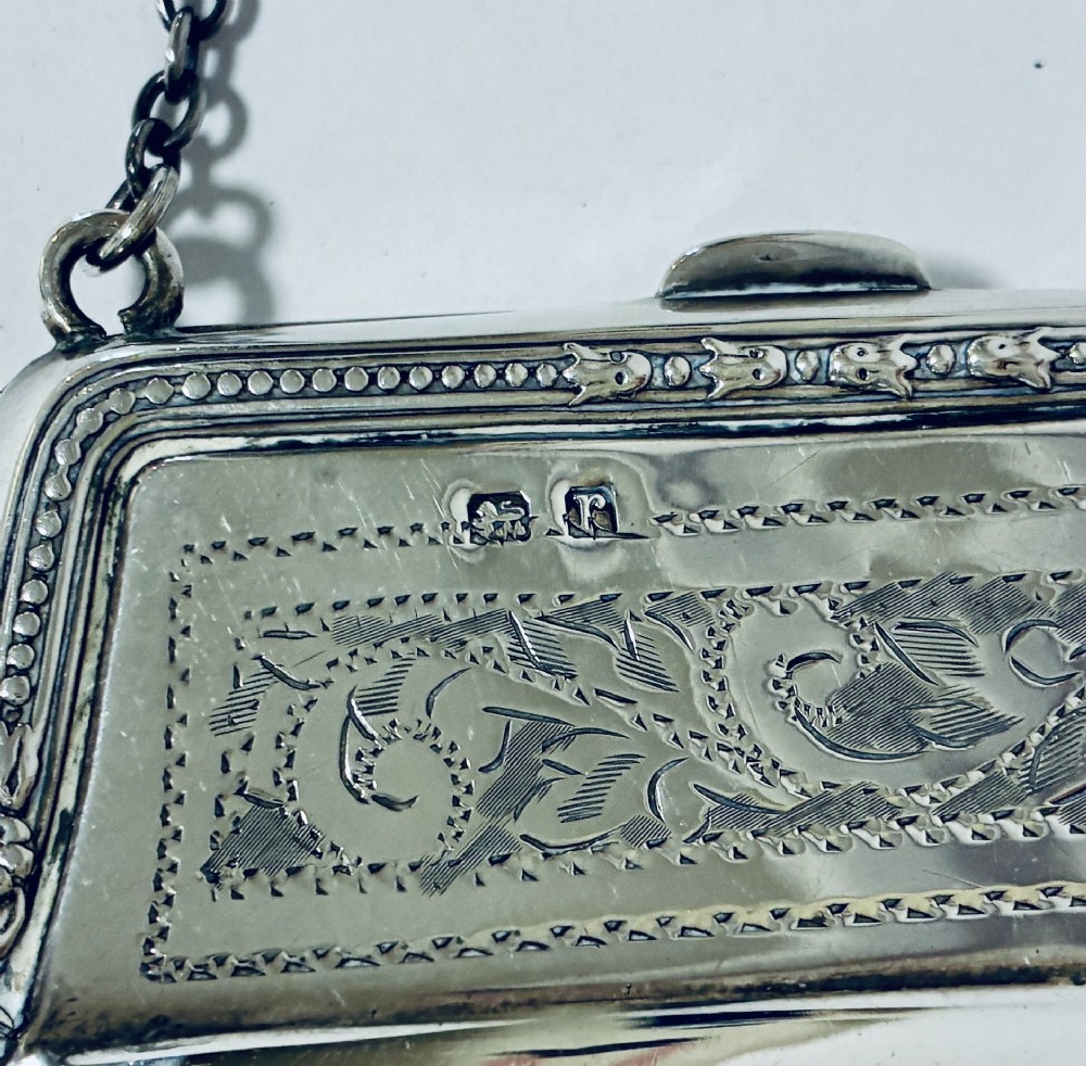 An antique sterling silver evening purse featuring engraved floral scrollwork, visible hallmarks along the upper frame, and a chain handle with a finger ring. View VIII