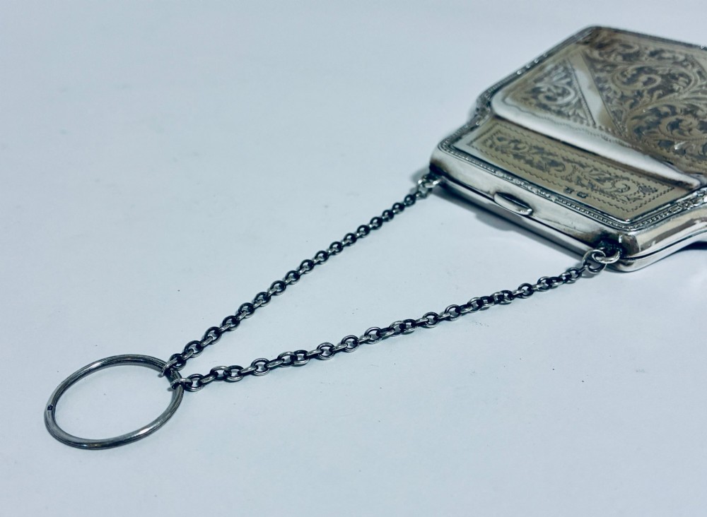 An antique sterling silver evening purse featuring engraved floral scrollwork, visible hallmarks along the upper frame, and a chain handle with a finger ring. View IX