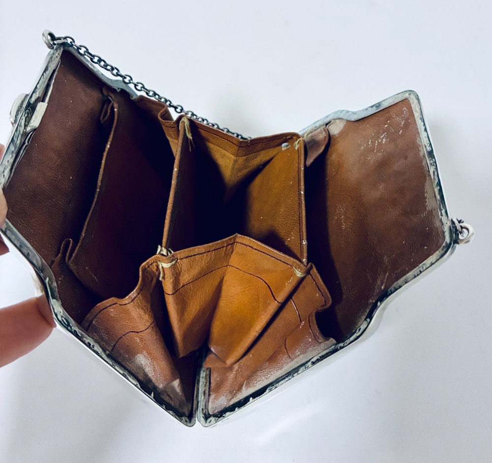 An antique sterling silver evening purse featuring engraved floral scrollwork, visible hallmarks along the upper frame, and a chain handle with a finger ring. View XI