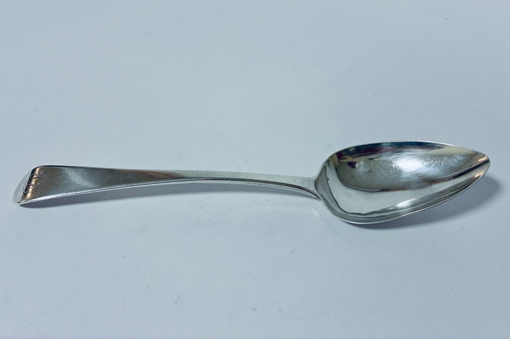 An antique sterling silver serving spoon featuring a tapered handle with monogram engraving and an oval bowl.