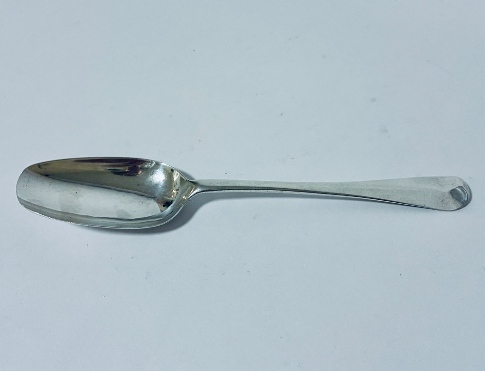 An 18th-century sterling silver serving spoon with a wide oval bowl and a smooth stem handle resting on a plain background.