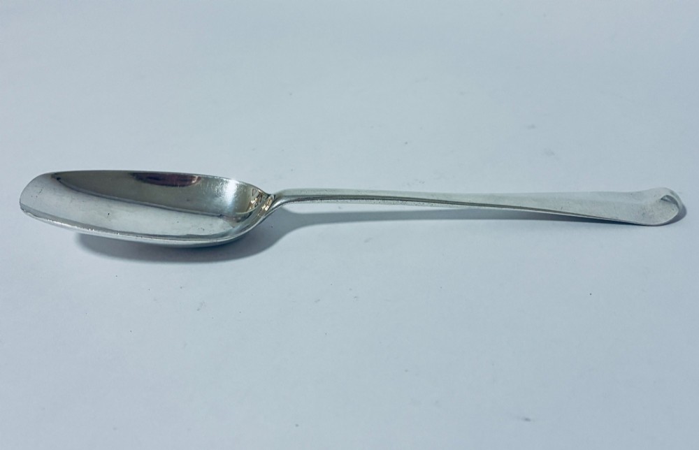 An 18th-century sterling silver serving spoon with a wide oval bowl and a smooth stem handle resting on a plain background. View II