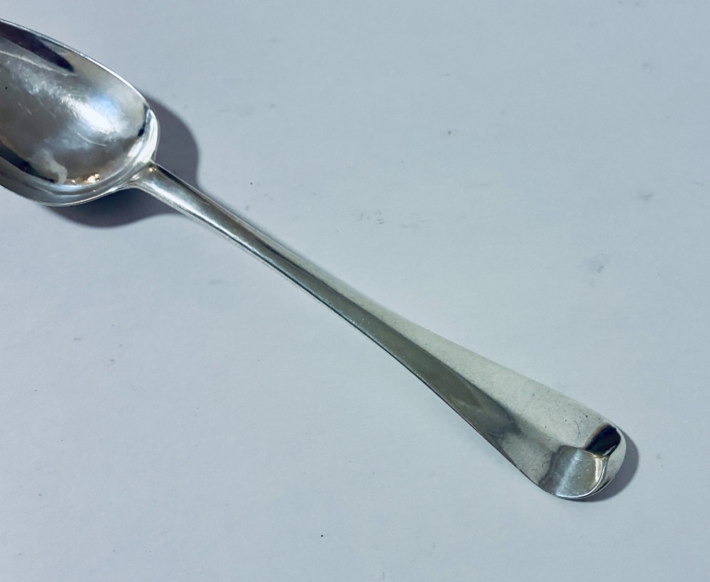 An 18th-century sterling silver serving spoon with a wide oval bowl and a smooth stem handle resting on a plain background. View III