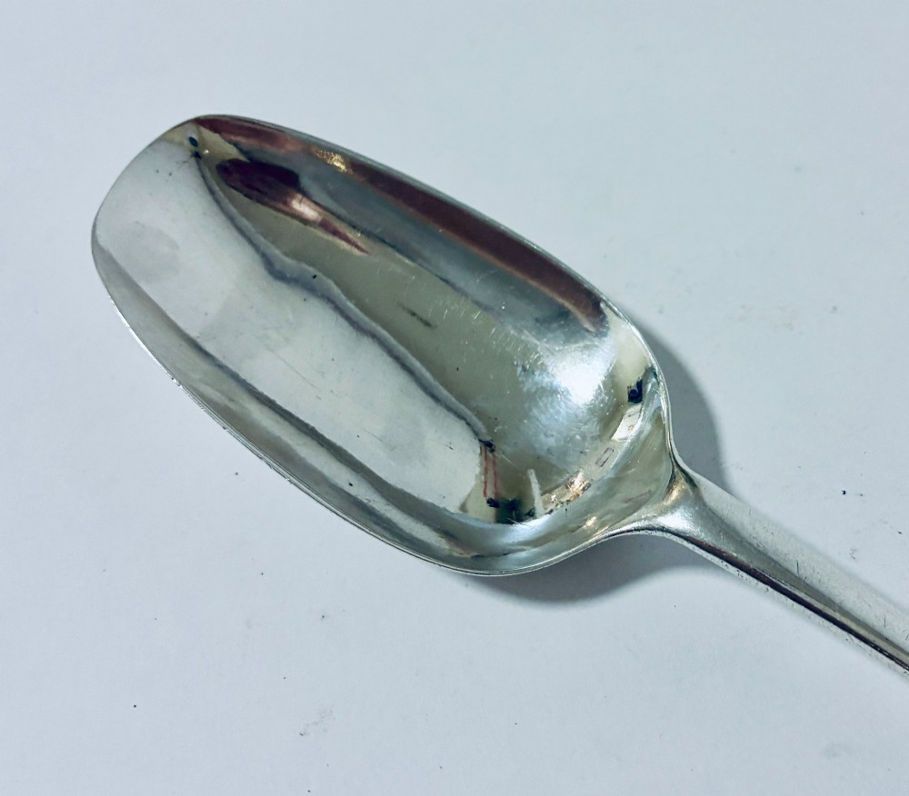 An 18th-century sterling silver serving spoon with a wide oval bowl and a smooth stem handle resting on a plain background. View IV