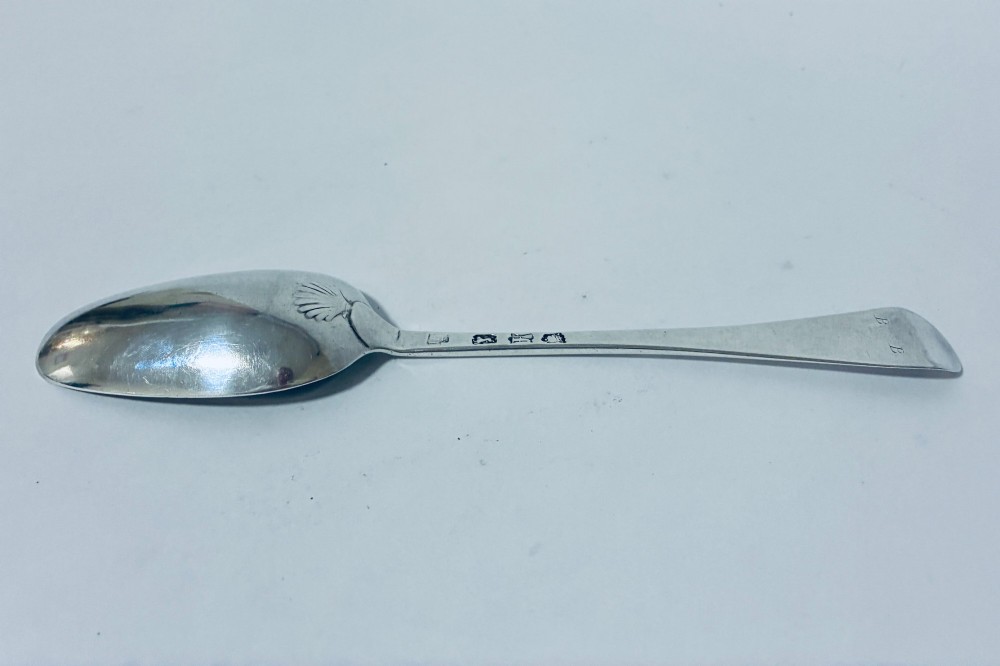 An 18th-century sterling silver serving spoon with a wide oval bowl and a smooth stem handle resting on a plain background. View V
