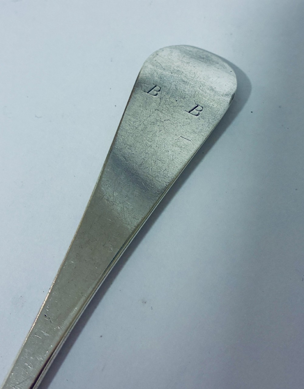 An 18th-century sterling silver serving spoon with a wide oval bowl and a smooth stem handle resting on a plain background. View IX