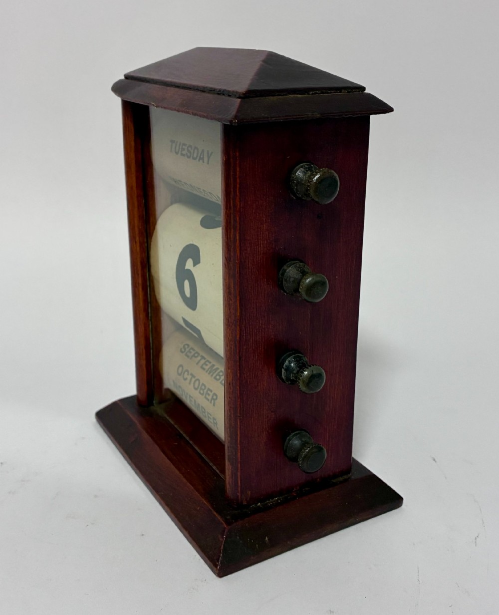 An antique wooden perpetual desk calendar featuring rotating printed scrolls for days, dates, and months displayed behind glass with turning knobs. View II