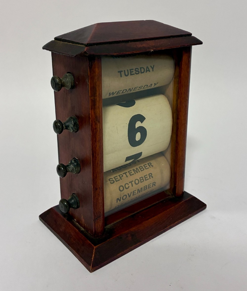An antique wooden perpetual desk calendar featuring rotating printed scrolls for days, dates, and months displayed behind glass with turning knobs. View VI