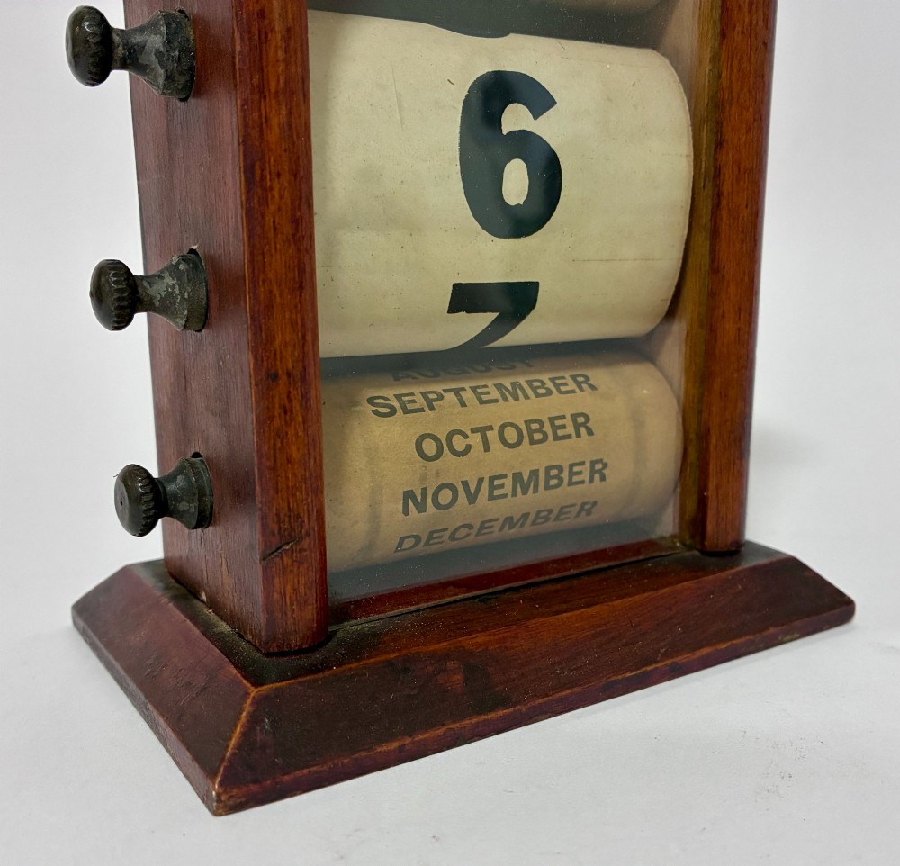 An antique wooden perpetual desk calendar featuring rotating printed scrolls for days, dates, and months displayed behind glass with turning knobs. View VIII