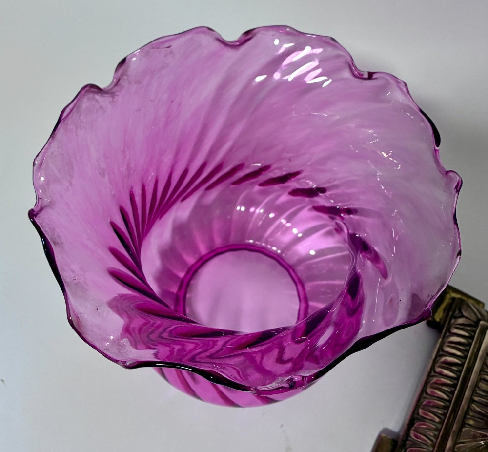 A Victorian oil lamp featuring a swirl optique cranberry glass shade and reservoir set atop a brass column and relief-moulded square base. View V