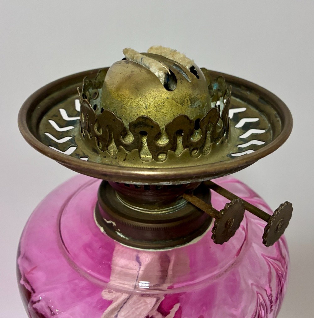 A Victorian oil lamp featuring a swirl optique cranberry glass shade and reservoir set atop a brass column and relief-moulded square base. View VII