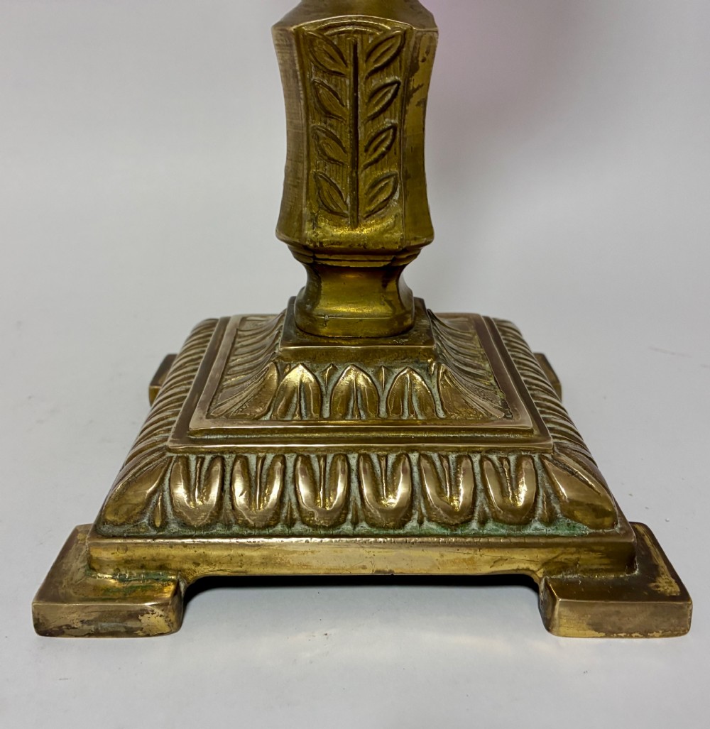 A Victorian oil lamp featuring a swirl optique cranberry glass shade and reservoir set atop a brass column and relief-moulded square base. View VIII