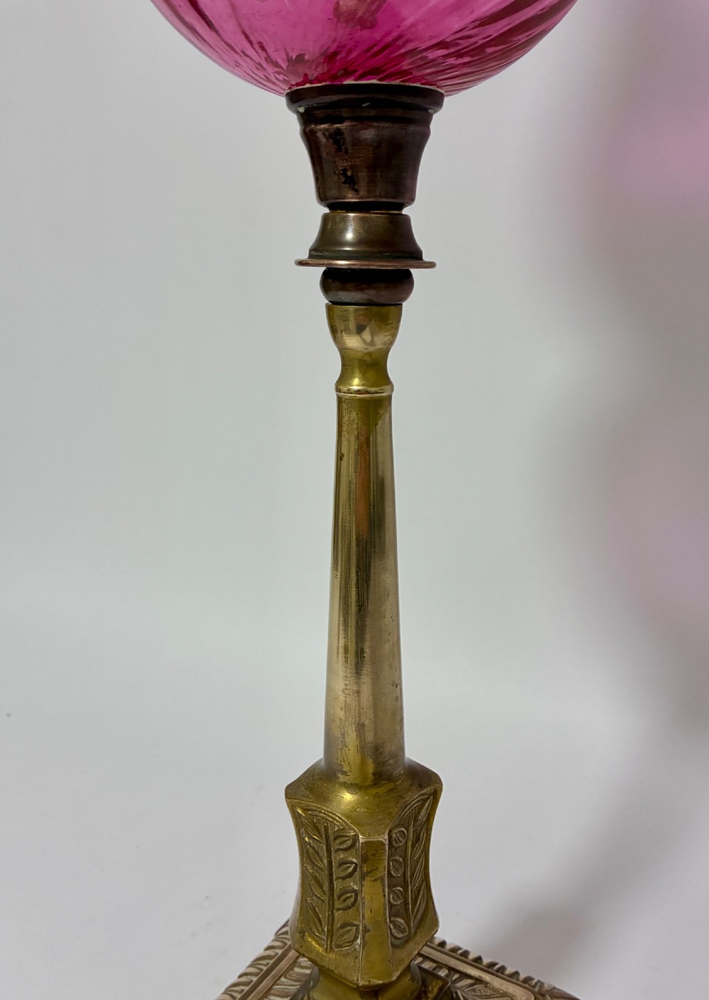 A Victorian oil lamp featuring a swirl optique cranberry glass shade and reservoir set atop a brass column and relief-moulded square base. View X