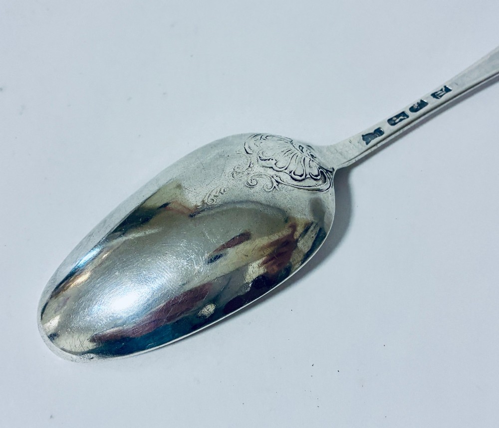 An 18th-century solid silver serving spoon featuring a plain tapered handle and an oval bowl. View X