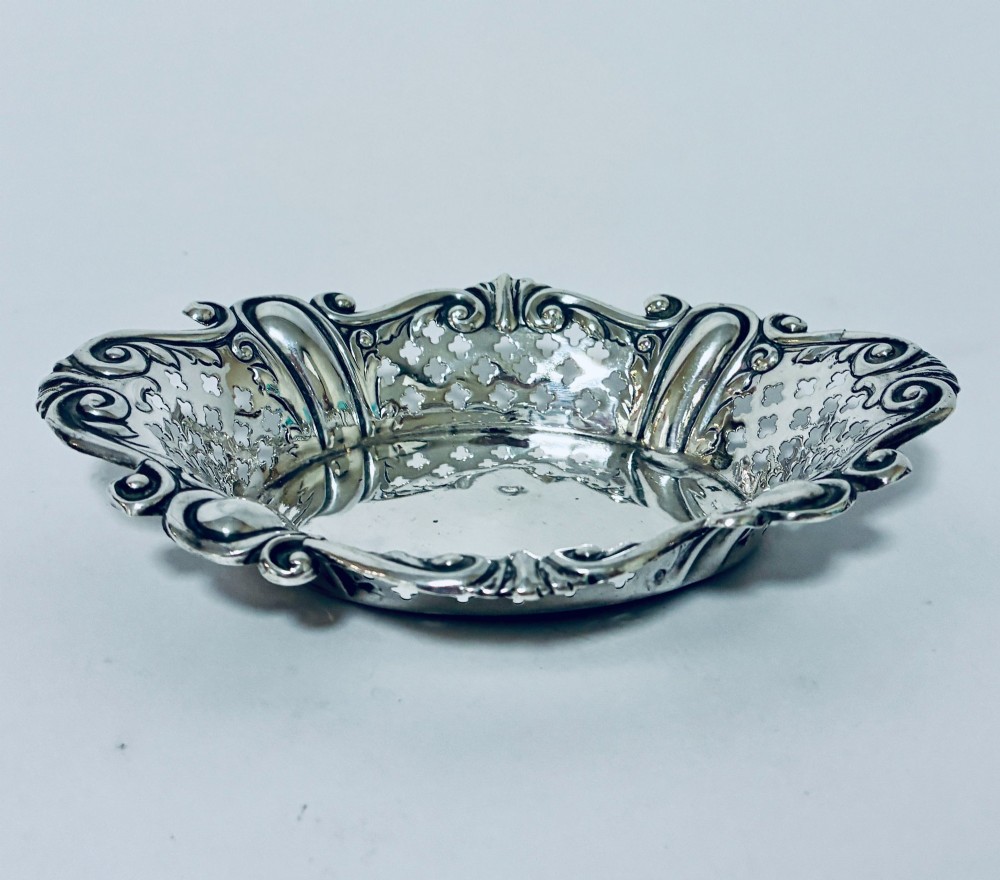An oval antique silver bonbon dish featuring intricately pierced fretwork sides and a scrolled rim.