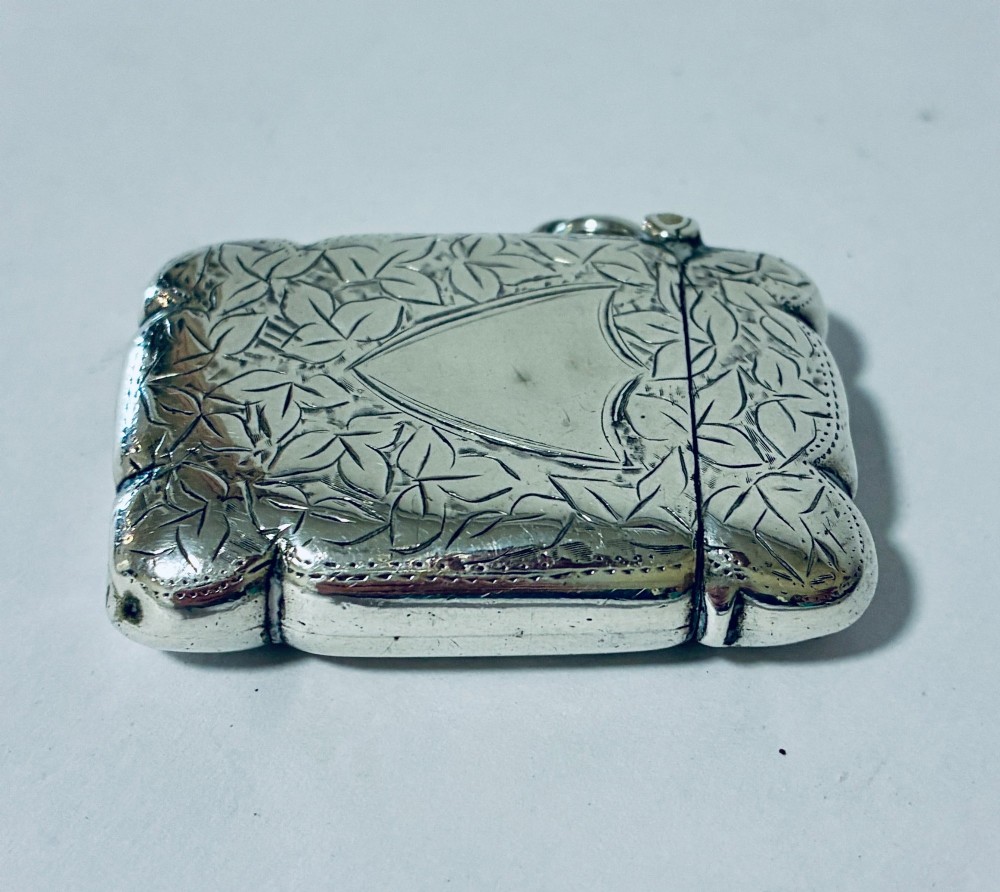 A Victorian sterling silver vesta case featuring hand-engraved foliage motifs, a central shield cartouche, lobed edges, and a side attachment ring. View III