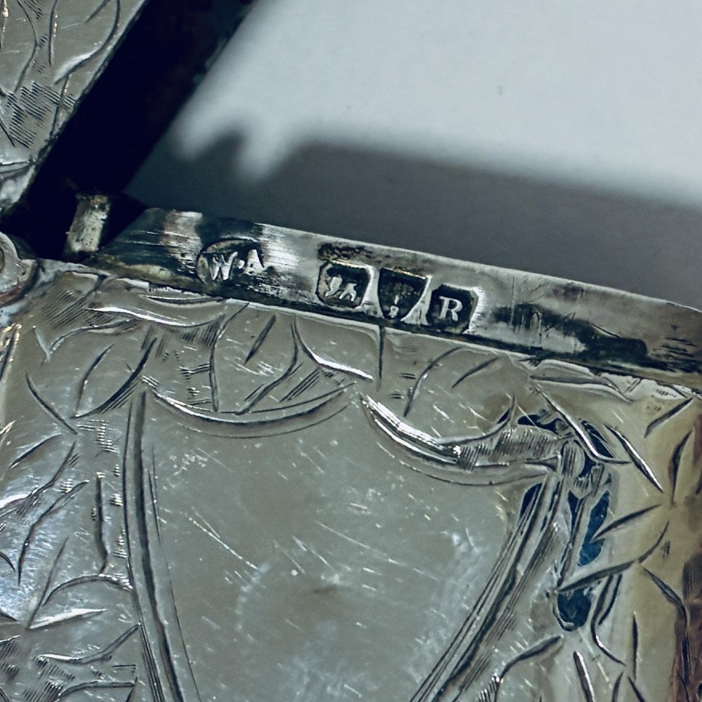 A Victorian sterling silver vesta case featuring hand-engraved foliage motifs, a central shield cartouche, lobed edges, and a side attachment ring. View IX