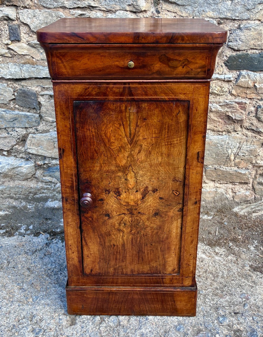 An antique French walnut pot cupboard with a figured burr walnut door panel, frieze drawer, and plinth base.