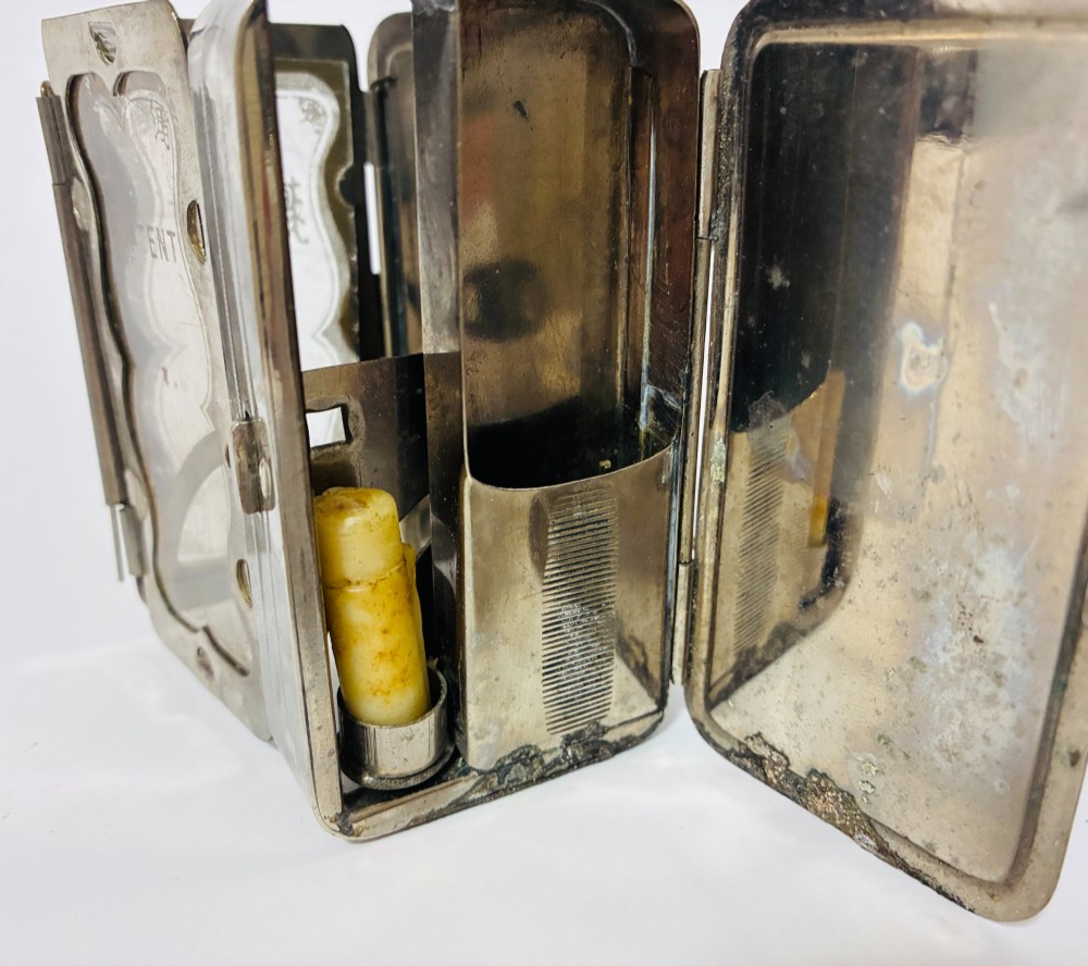 An open nickel-plated folding pocket lantern containing a small wax candle and a glass panel stamped with patent text. View II