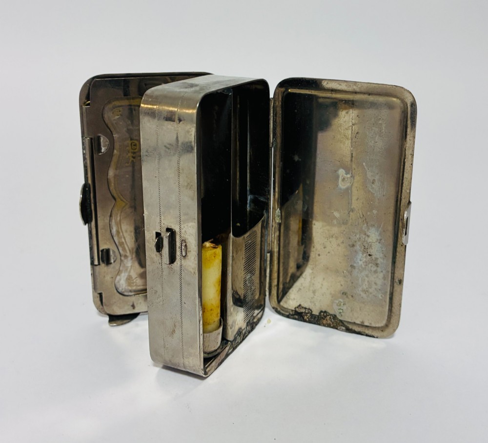 An open nickel-plated folding pocket lantern containing a small wax candle and a glass panel stamped with patent text. View XII