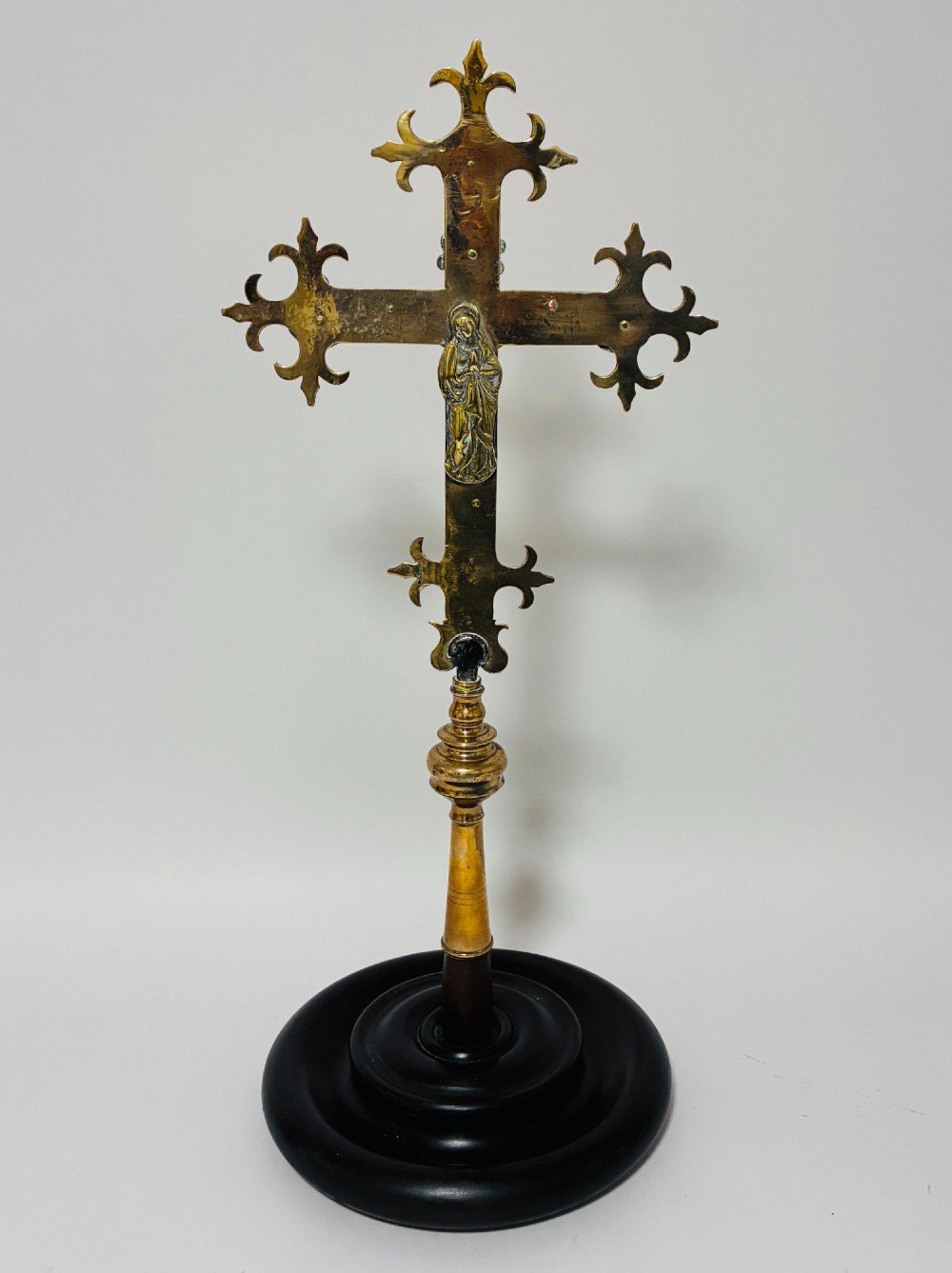 An antique brass processional cross featuring a detailed crucifix figure, fleur-de-lis terminal accents, and engraved motifs, mounted on a turned dark wood stand. View XI