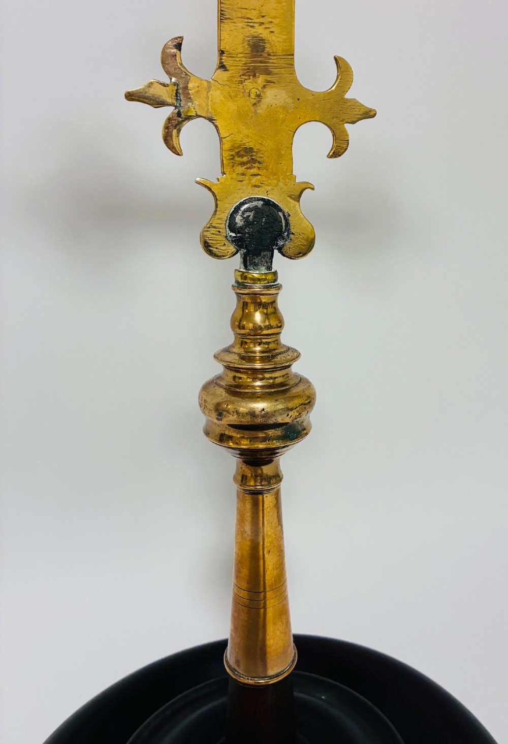 An antique brass processional cross featuring a detailed crucifix figure, fleur-de-lis terminal accents, and engraved motifs, mounted on a turned dark wood stand. View XIV