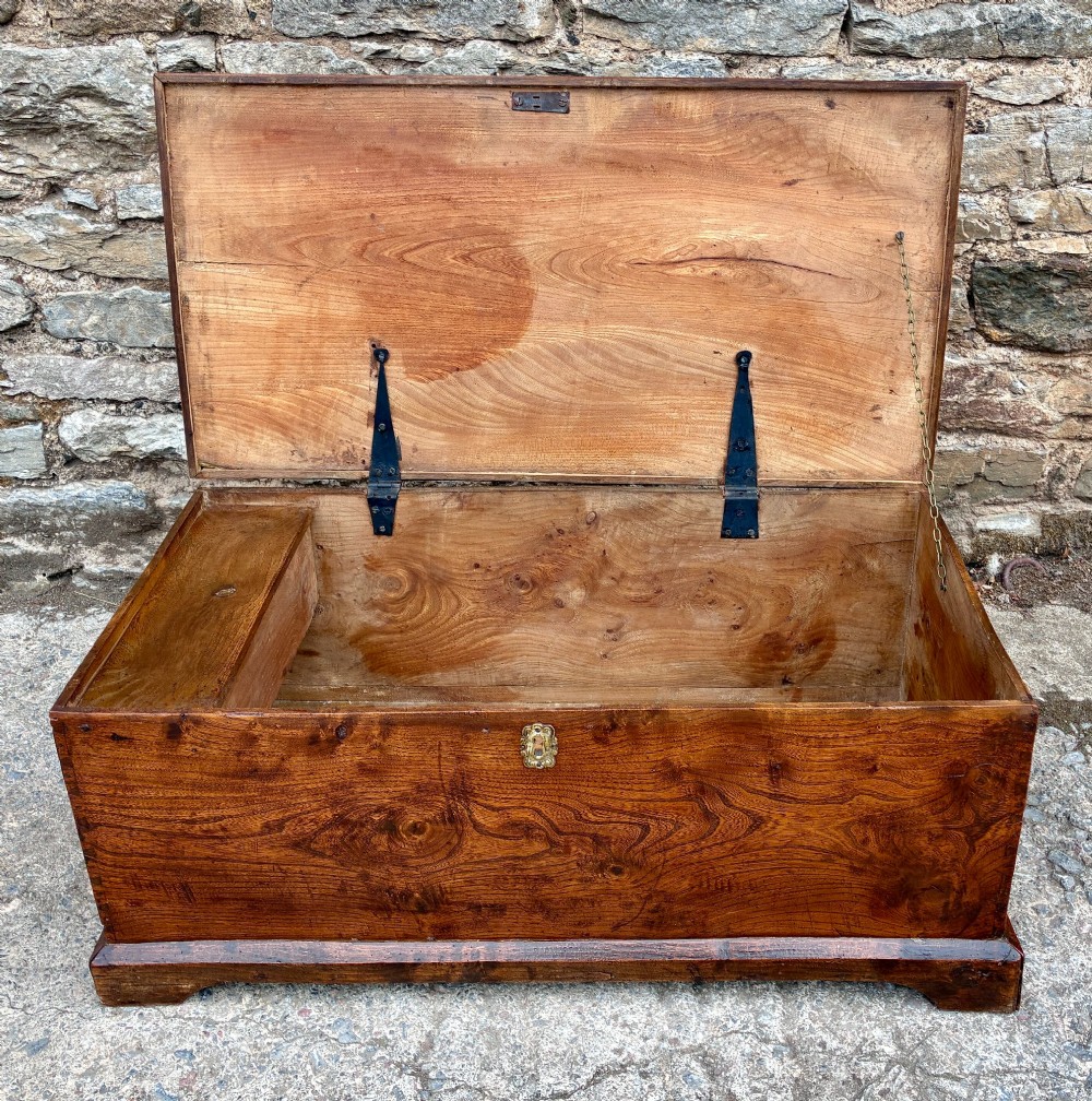 A low rectangular warm brown elm blanket box featuring a hinged top, polished finish, brass keyhole escutcheon, and bracket feet. View III