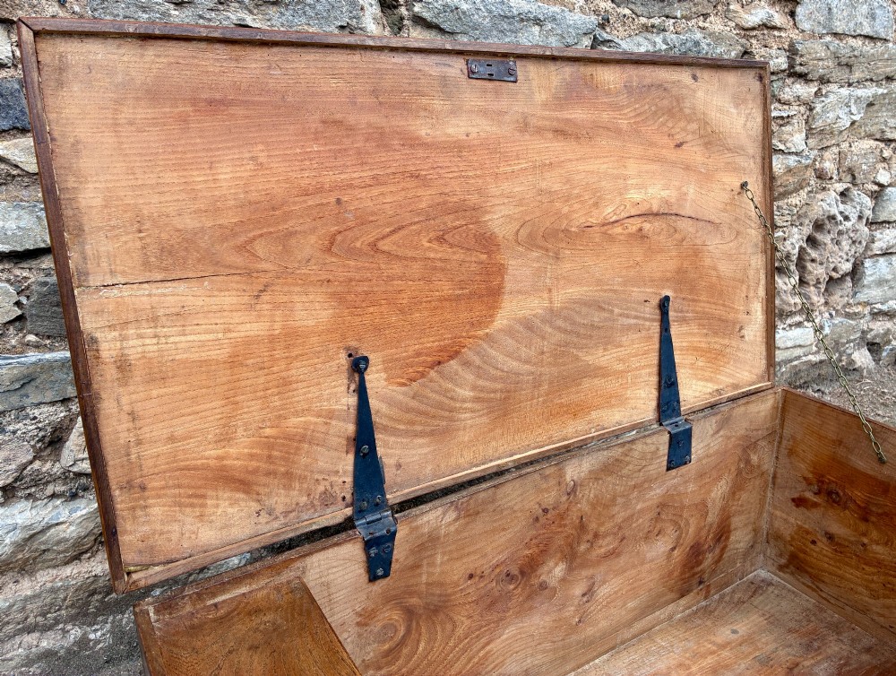 A low rectangular warm brown elm blanket box featuring a hinged top, polished finish, brass keyhole escutcheon, and bracket feet. View V