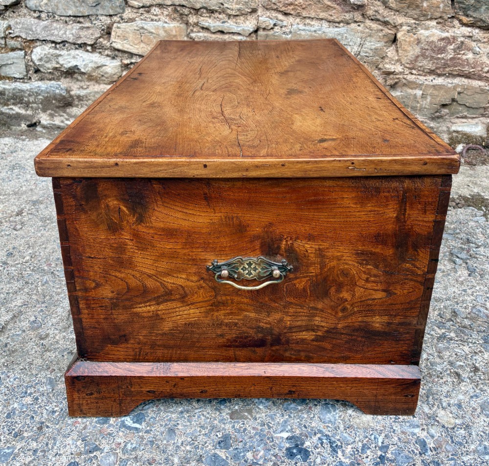 A low rectangular warm brown elm blanket box featuring a hinged top, polished finish, brass keyhole escutcheon, and bracket feet. View IX