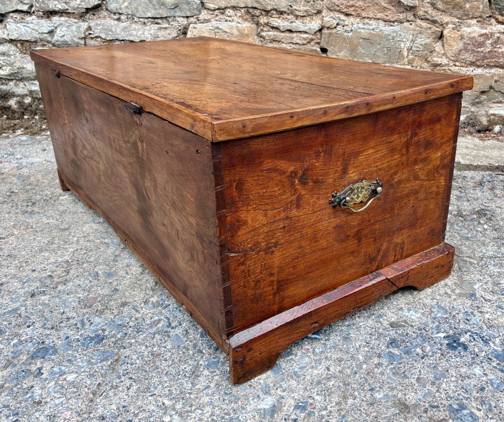 A low rectangular warm brown elm blanket box featuring a hinged top, polished finish, brass keyhole escutcheon, and bracket feet. View XII