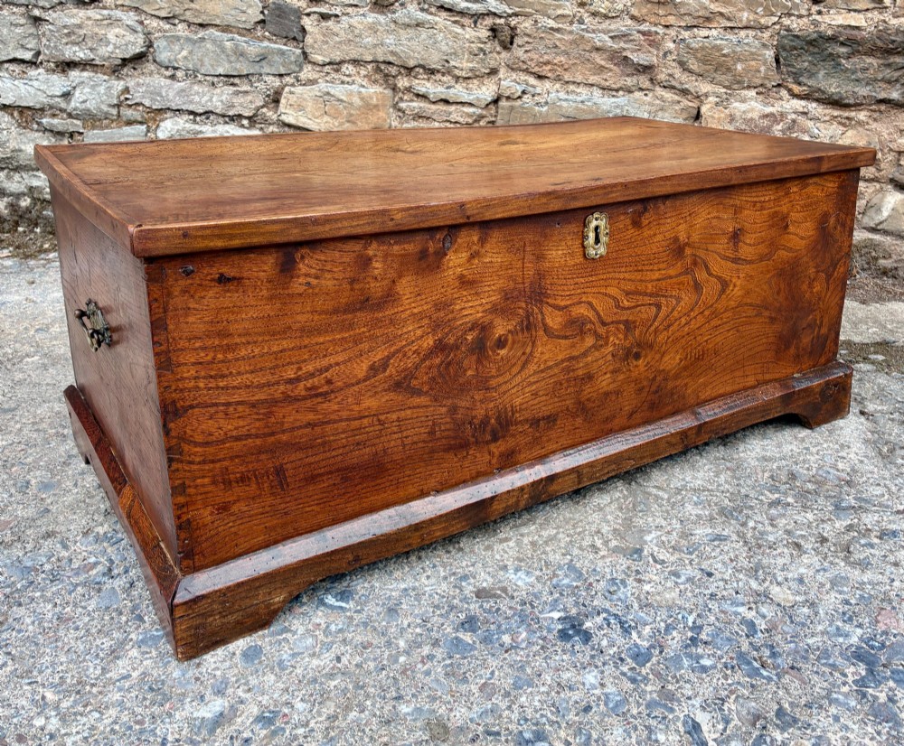 A low rectangular warm brown elm blanket box featuring a hinged top, polished finish, brass keyhole escutcheon, and bracket feet. View XIV