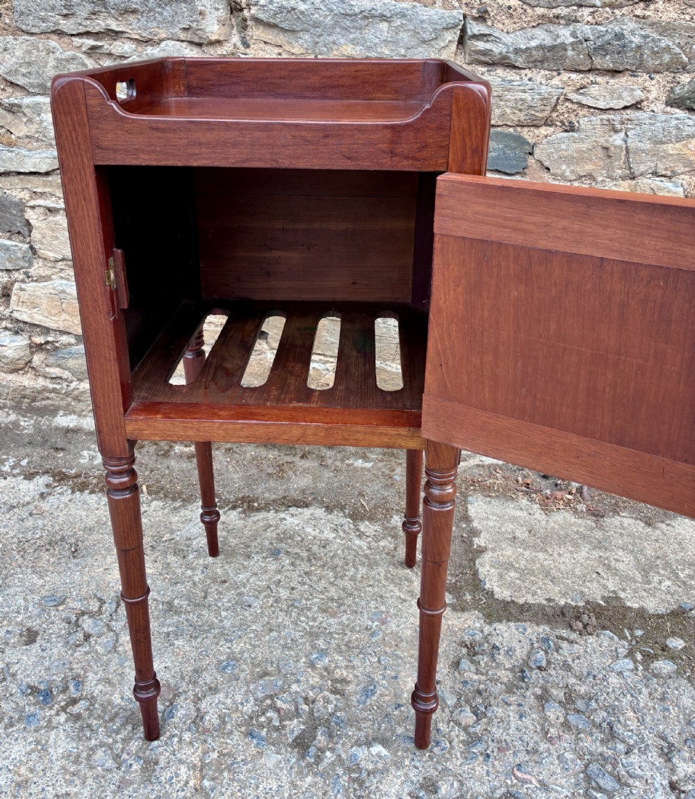 A Georgian mahogany pot cupboard featuring a tray top gallery with cut-out handles, a single veneered door, and turned legs. View IV