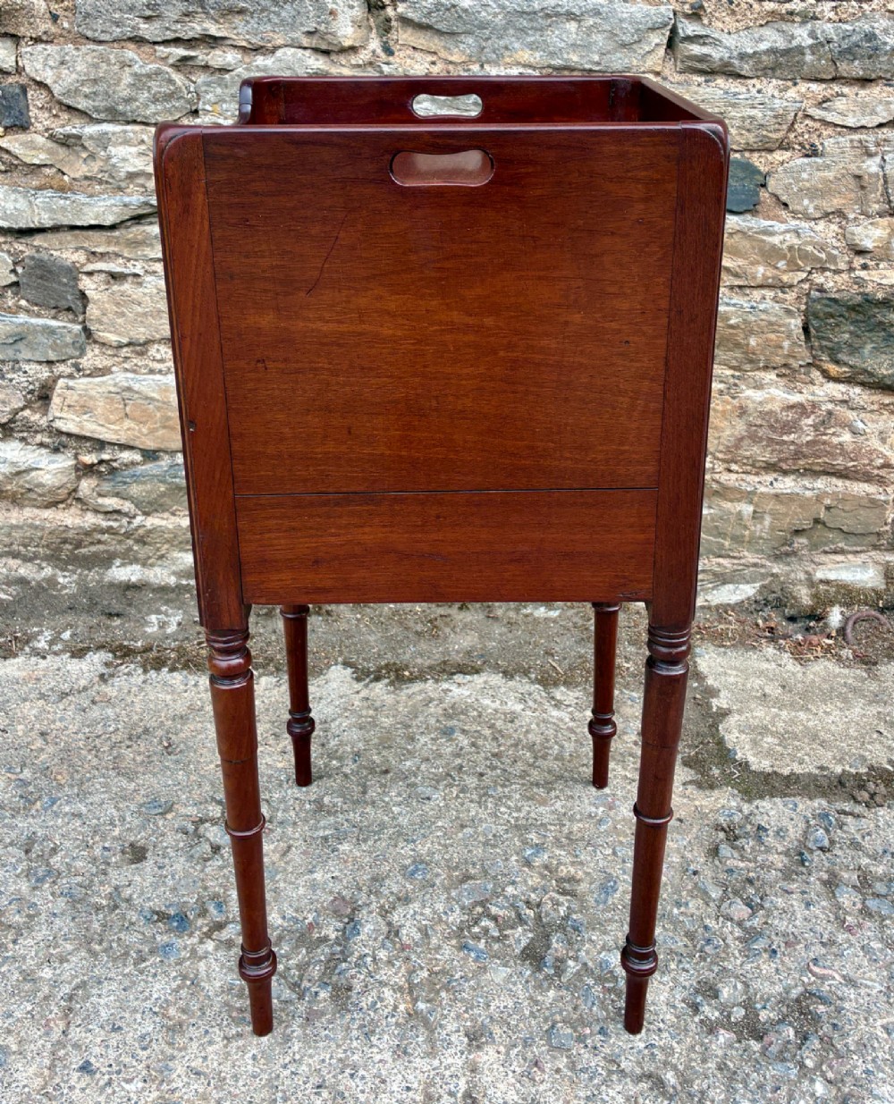 A Georgian mahogany pot cupboard featuring a tray top gallery with cut-out handles, a single veneered door, and turned legs. View VII