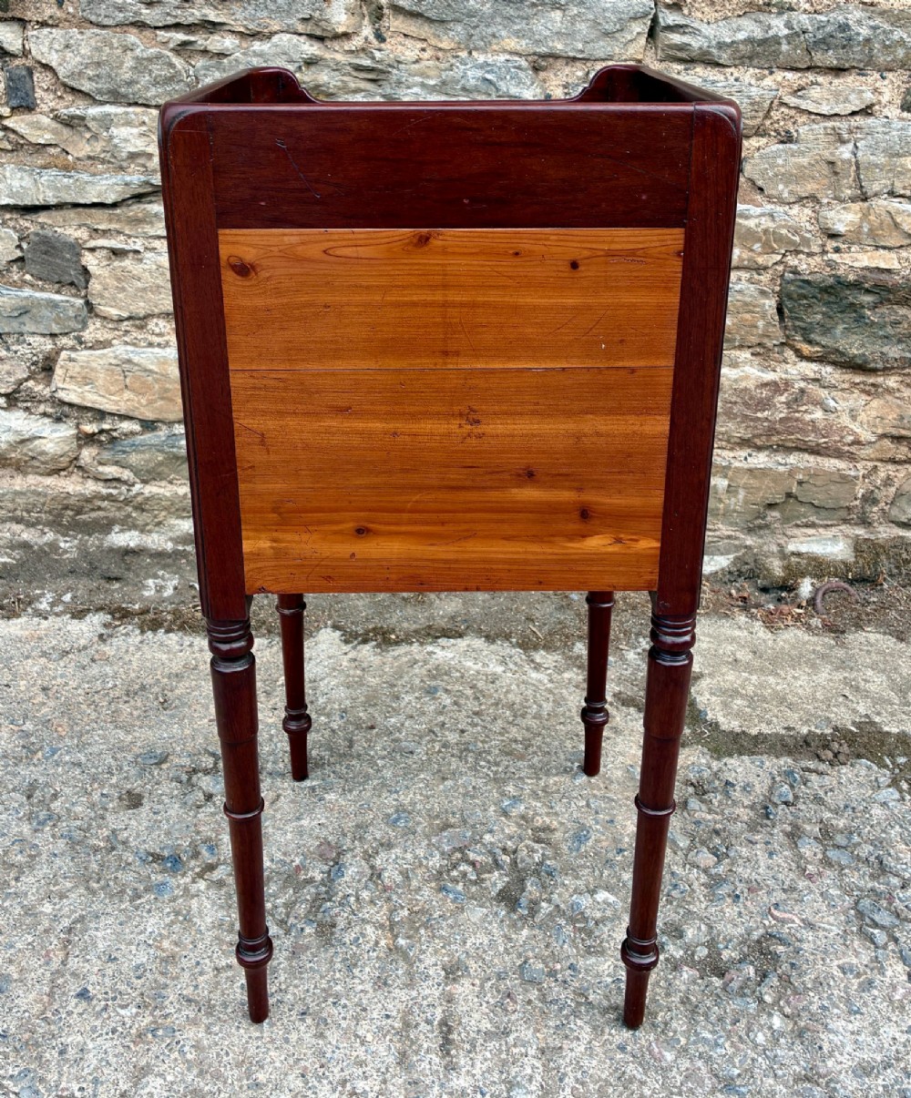A Georgian mahogany pot cupboard featuring a tray top gallery with cut-out handles, a single veneered door, and turned legs. View VIII