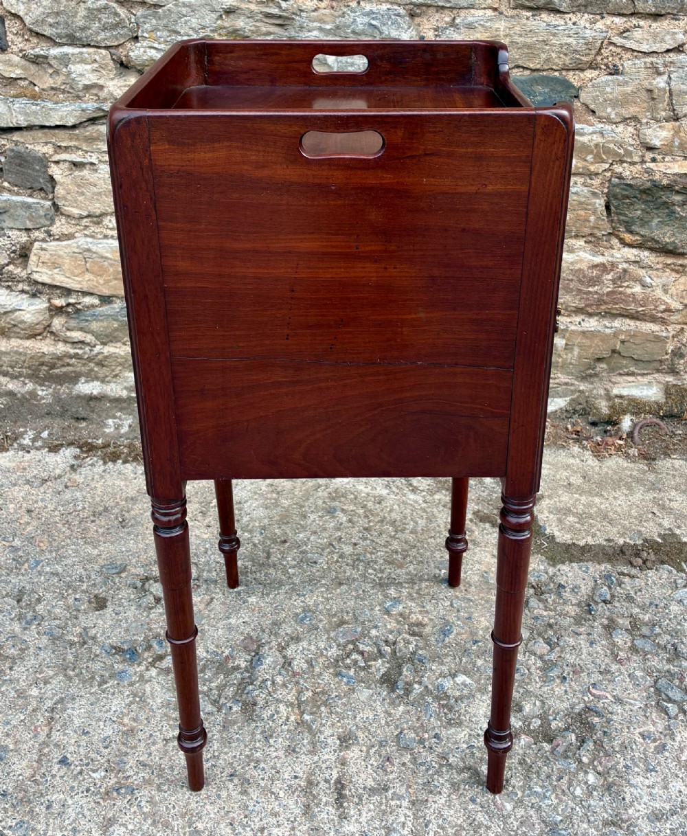 A Georgian mahogany pot cupboard featuring a tray top gallery with cut-out handles, a single veneered door, and turned legs. View IX