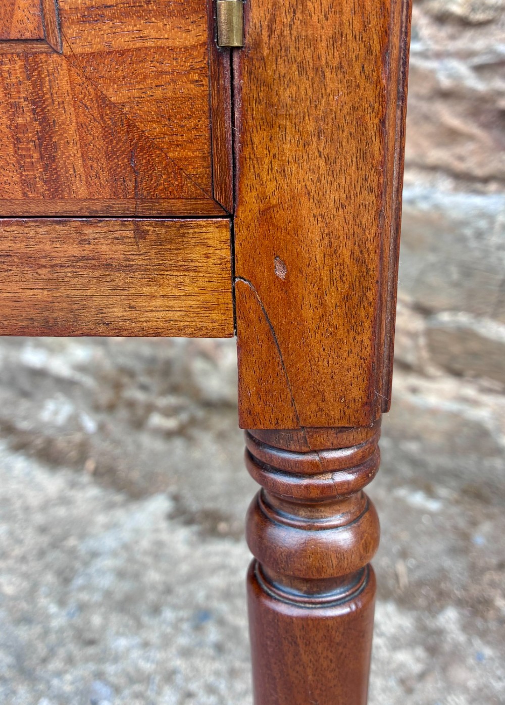A Georgian mahogany pot cupboard featuring a tray top gallery with cut-out handles, a single veneered door, and turned legs. View XII