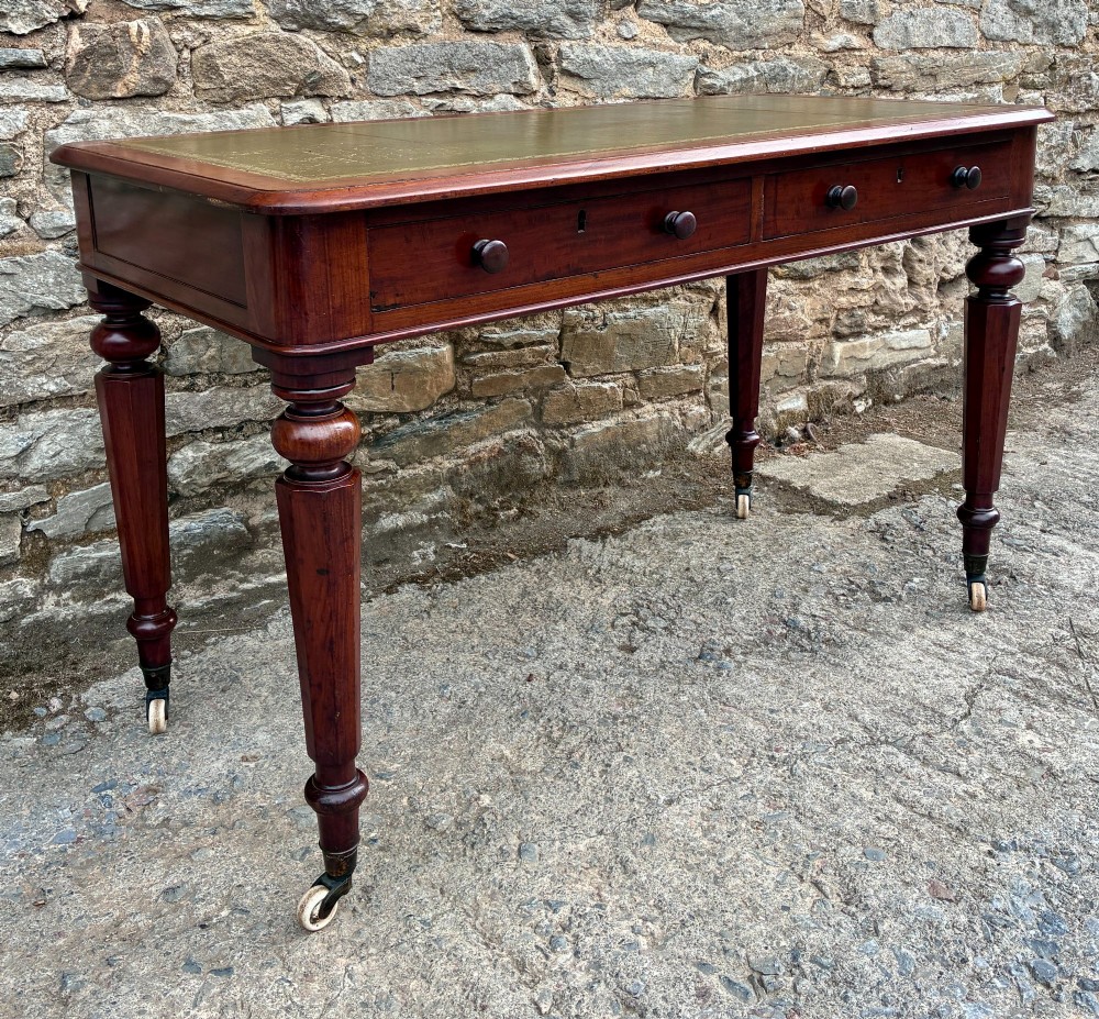 A Victorian mahogany writing table featuring a green gilt-tooled leather writing surface, two drawers with turned knob handles, and turned tapered legs resting on ceramic castors. View III