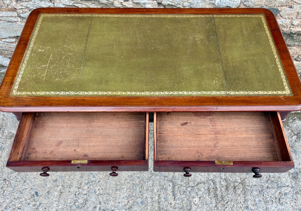 A Victorian mahogany writing table featuring a green gilt-tooled leather writing surface, two drawers with turned knob handles, and turned tapered legs resting on ceramic castors. View IV
