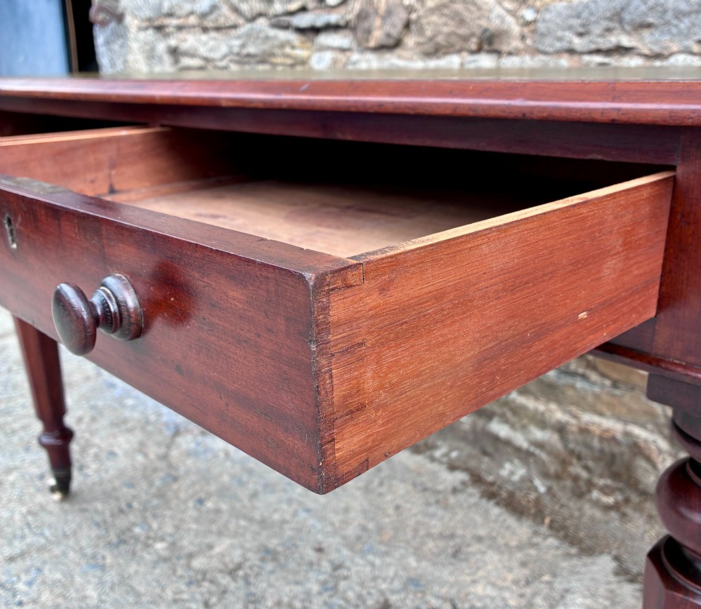 A Victorian mahogany writing table featuring a green gilt-tooled leather writing surface, two drawers with turned knob handles, and turned tapered legs resting on ceramic castors. View V