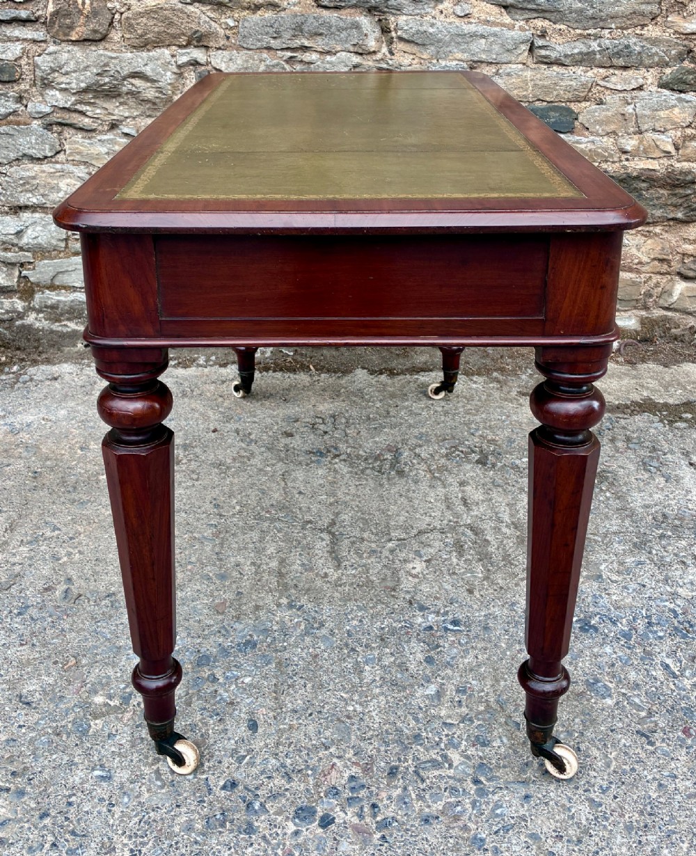 A Victorian mahogany writing table featuring a green gilt-tooled leather writing surface, two drawers with turned knob handles, and turned tapered legs resting on ceramic castors. View VII