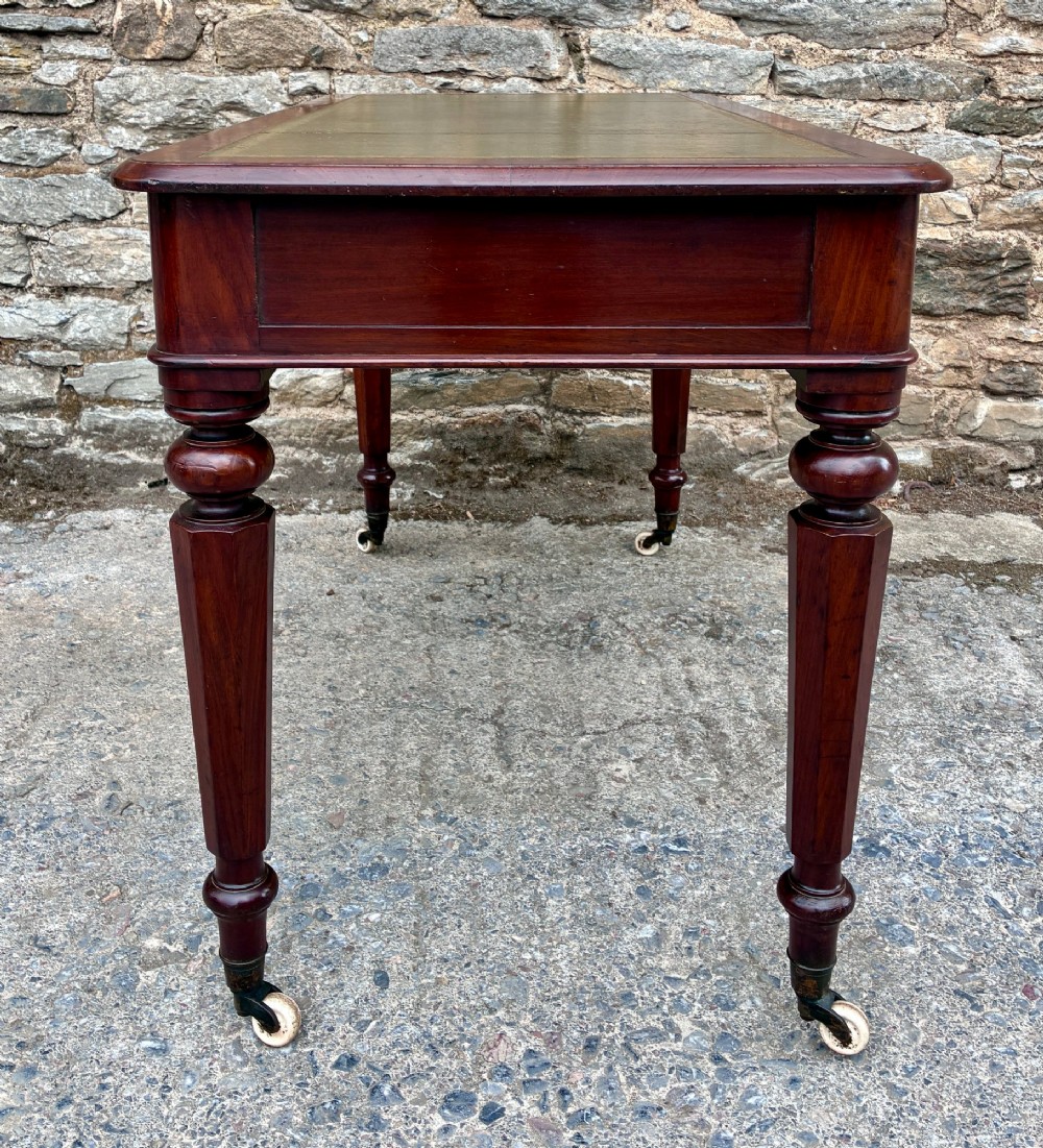 A Victorian mahogany writing table featuring a green gilt-tooled leather writing surface, two drawers with turned knob handles, and turned tapered legs resting on ceramic castors. View VIII