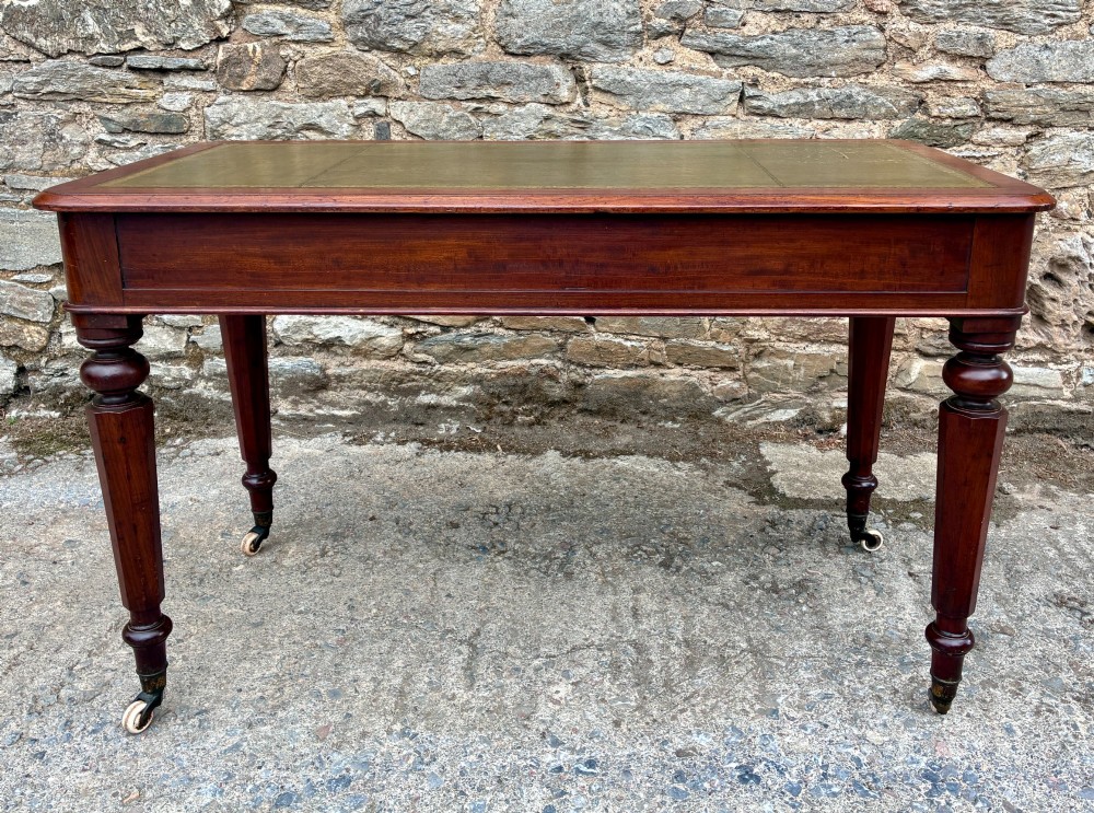 A Victorian mahogany writing table featuring a green gilt-tooled leather writing surface, two drawers with turned knob handles, and turned tapered legs resting on ceramic castors. View IX