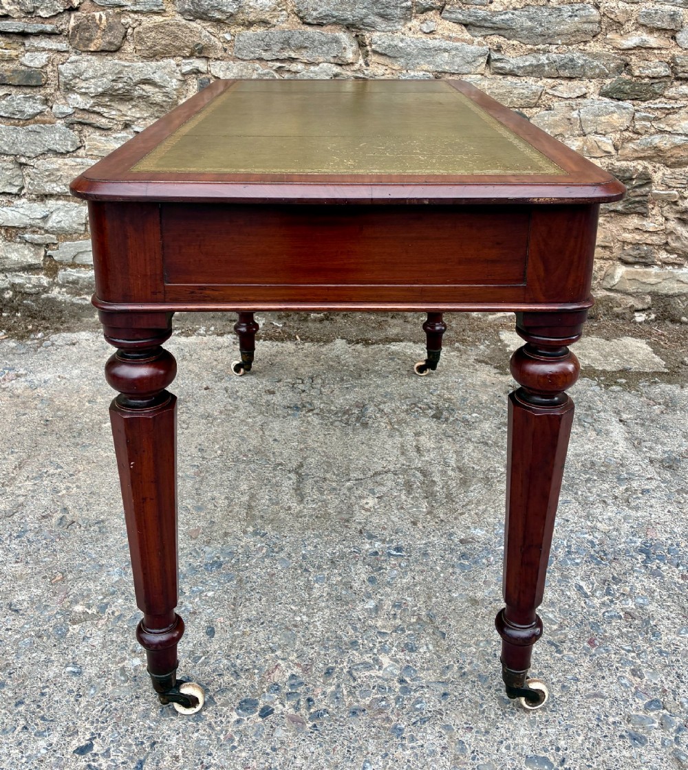 A Victorian mahogany writing table featuring a green gilt-tooled leather writing surface, two drawers with turned knob handles, and turned tapered legs resting on ceramic castors. View X