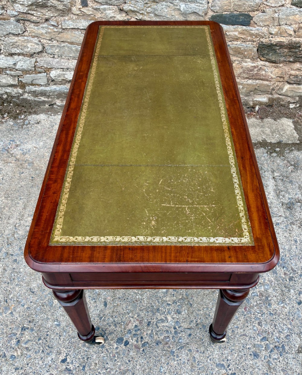 A Victorian mahogany writing table featuring a green gilt-tooled leather writing surface, two drawers with turned knob handles, and turned tapered legs resting on ceramic castors. View XI