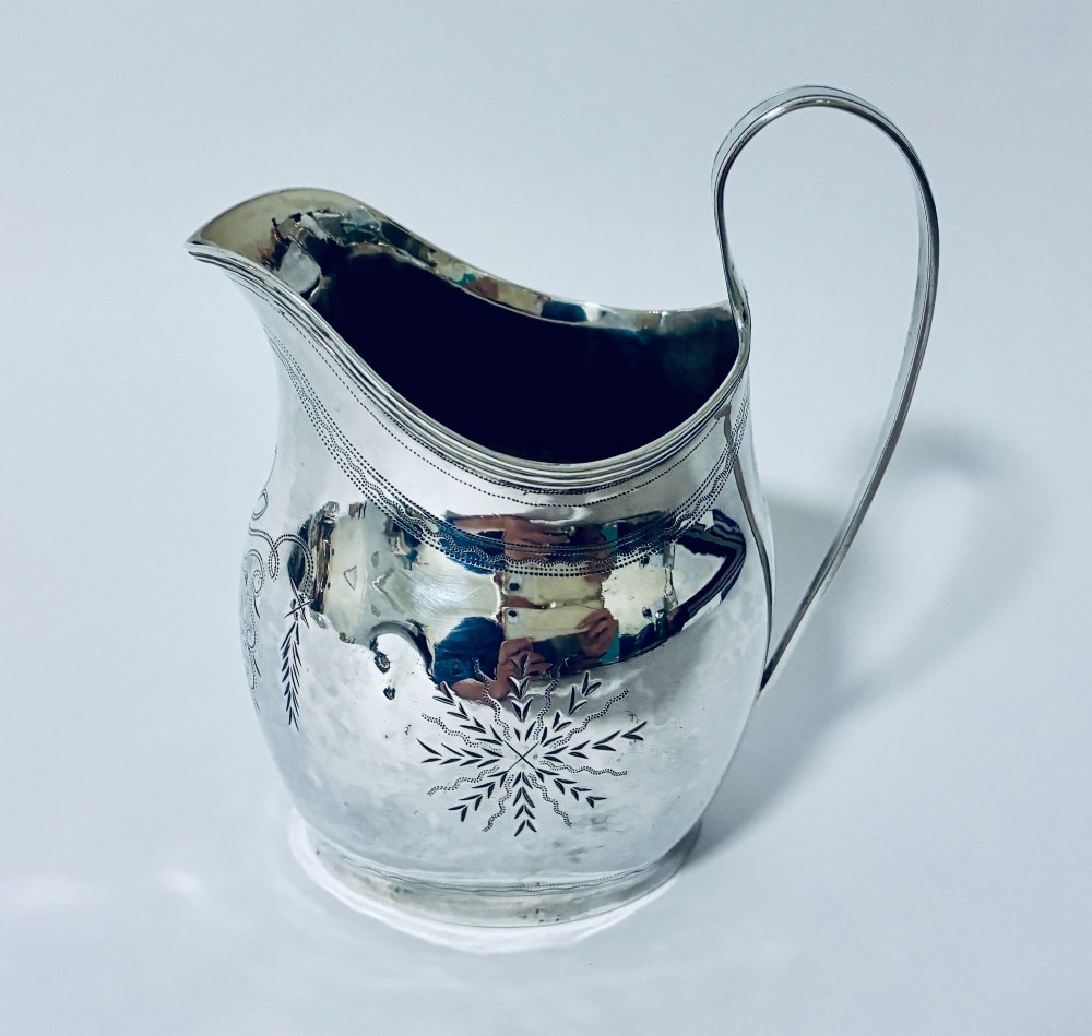 A Georgian sterling silver cream jug featuring a high loop handle, poured spout, and bright-cut star motif engraving on its body.