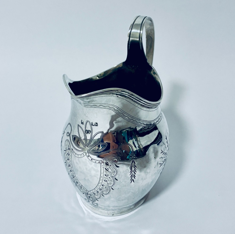 A Georgian sterling silver cream jug featuring a high loop handle, poured spout, and bright-cut star motif engraving on its body. View II