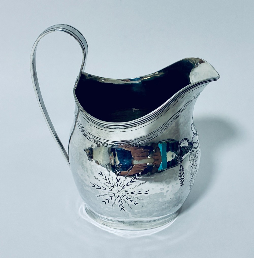 A Georgian sterling silver cream jug featuring a high loop handle, poured spout, and bright-cut star motif engraving on its body. View IV