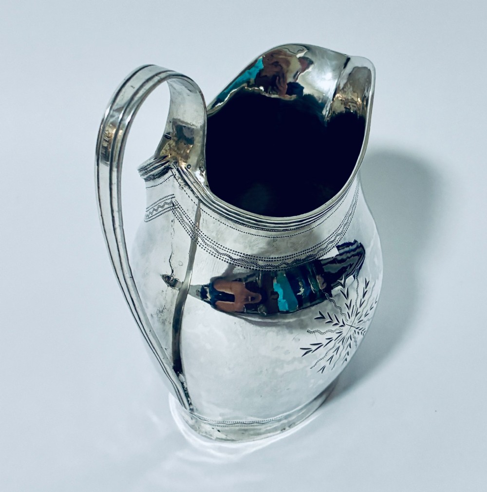A Georgian sterling silver cream jug featuring a high loop handle, poured spout, and bright-cut star motif engraving on its body. View V
